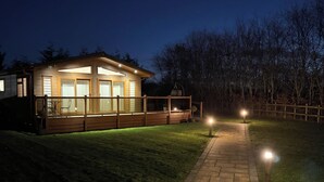 Eine Holzhütte mit einer Terrasse, einem Grillplatz und einem Weg zum Eingang.