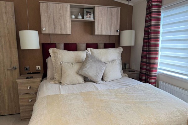 Une chambre à coucher comprenant un lit, deux tables de chevet, une armoire et une fenêtre avec des rideaux.
