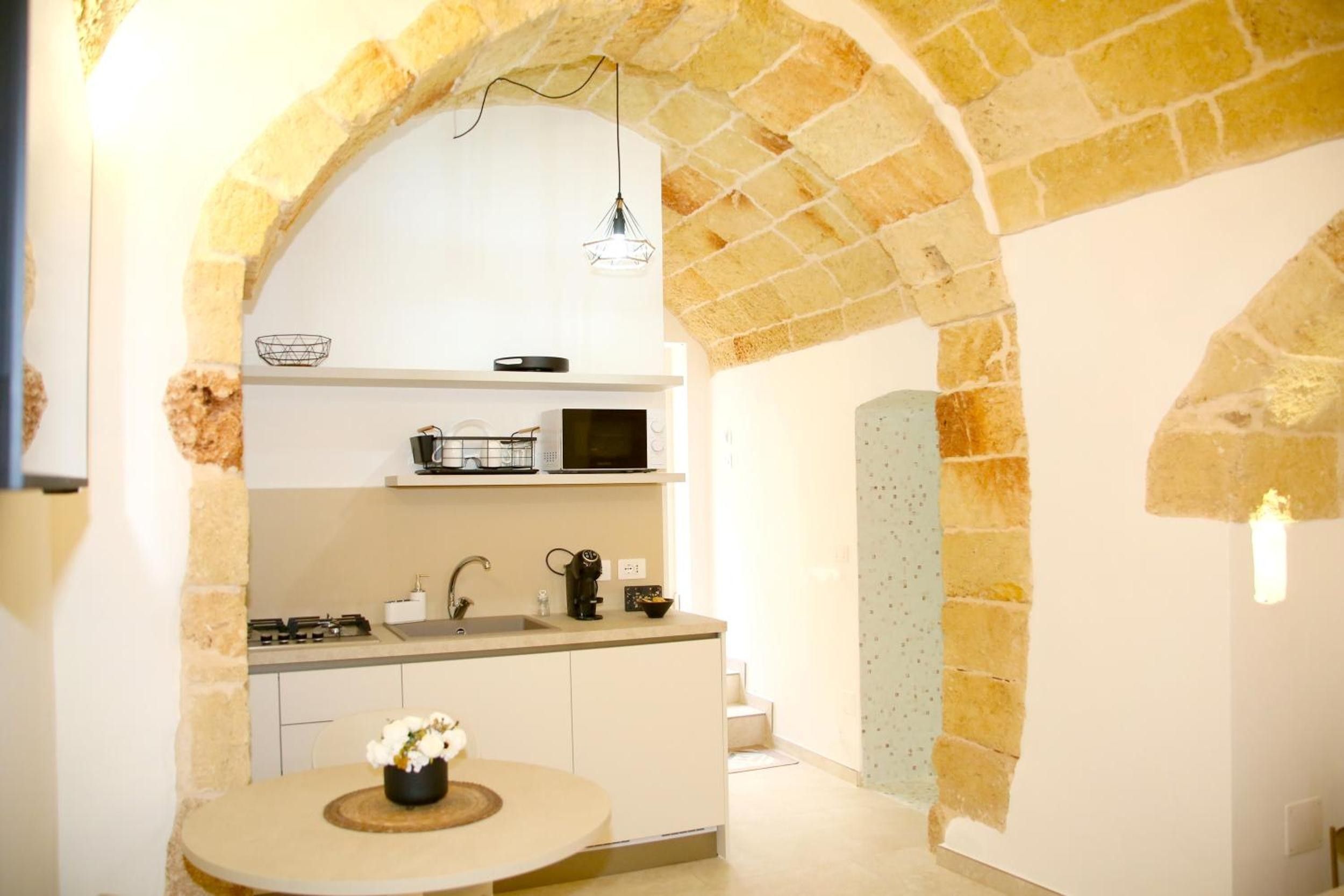 A kitchen with a stone archway, a round table with a vase of flowers, and a microwave above the counter.