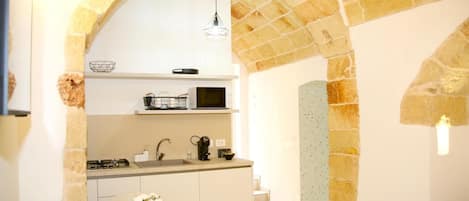 A kitchen with a stone archway, a round table with a vase of flowers, and a microwave above the counter.