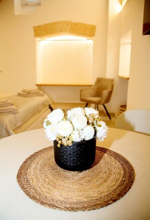 Een kamer met een bed, een stoel en een vaas met witte bloemen op een geweven mat.