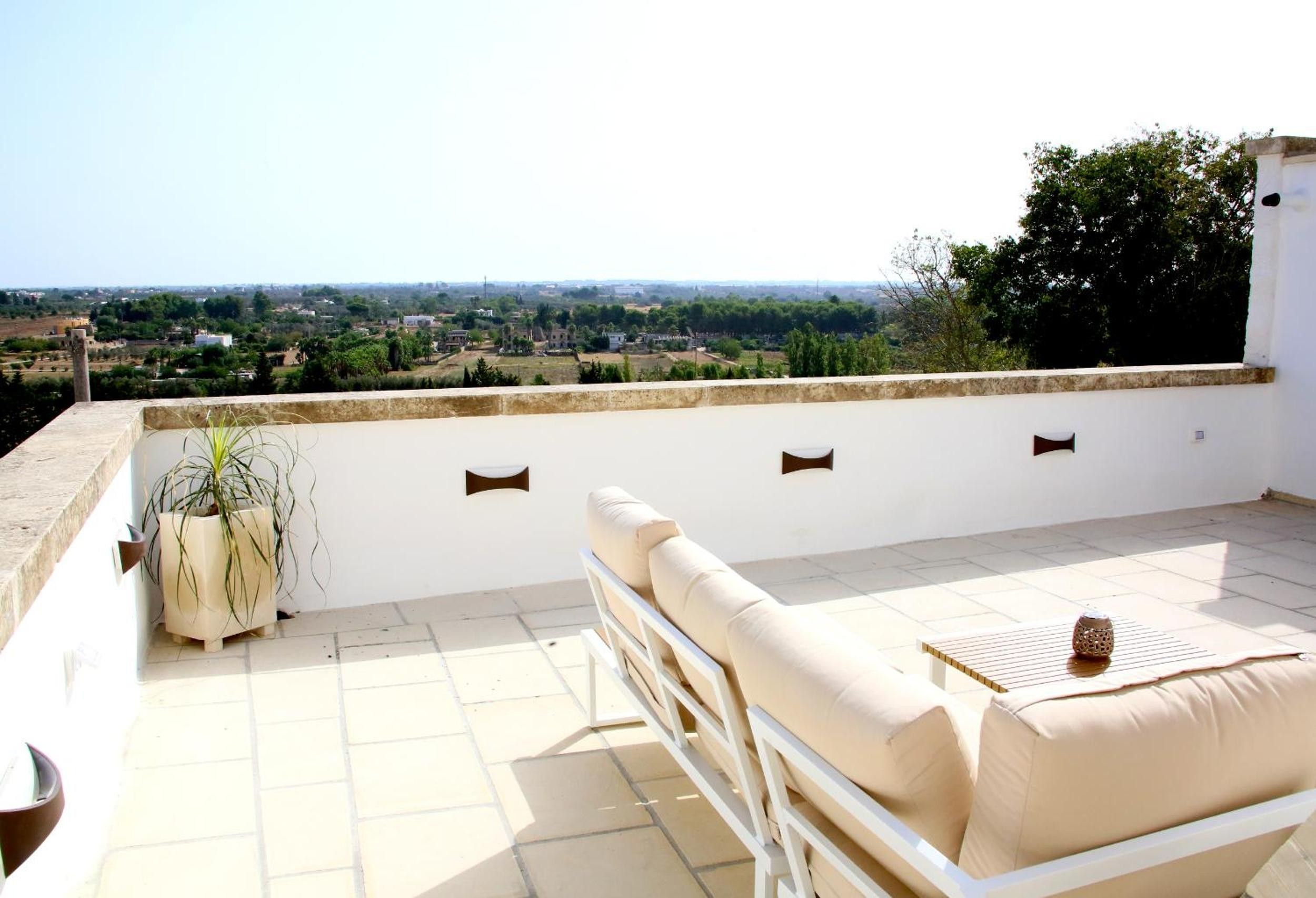 Eine Dachterrasse mit einer Couch und einem Blumentopf, mit Blick auf eine Stadtlandschaft.