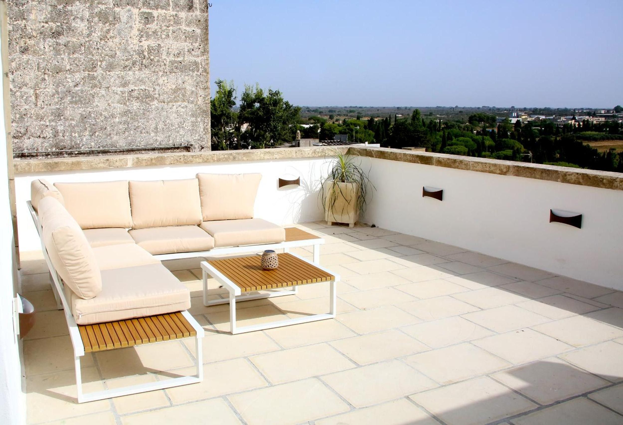 Eine Dachterrasse mit einem beigefarbenen Sofa, einem Holztisch und einem Blumentopf.