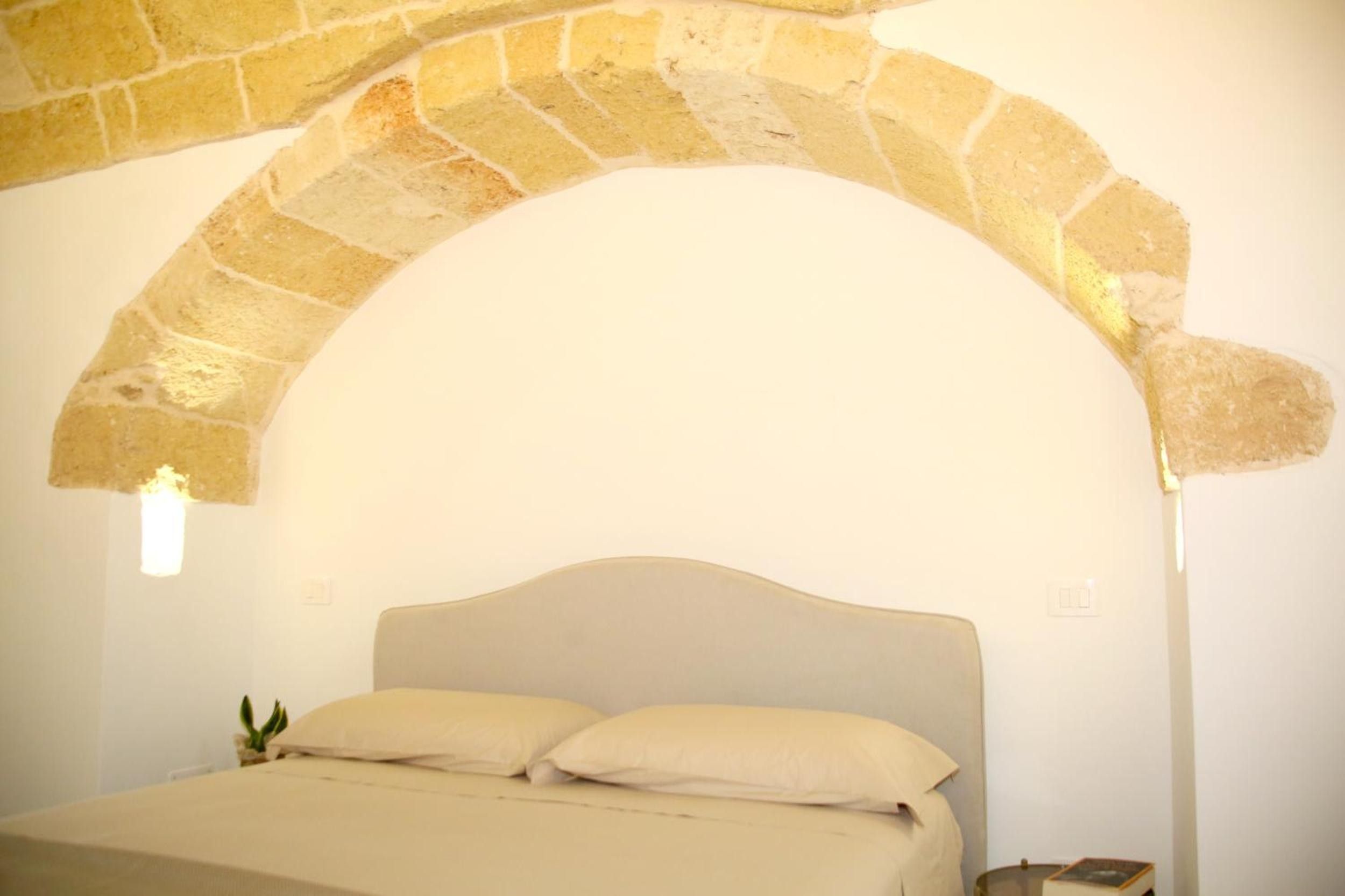 A bedroom with a stone archway, a bed with white bedding, and a bedside table with a lamp.
