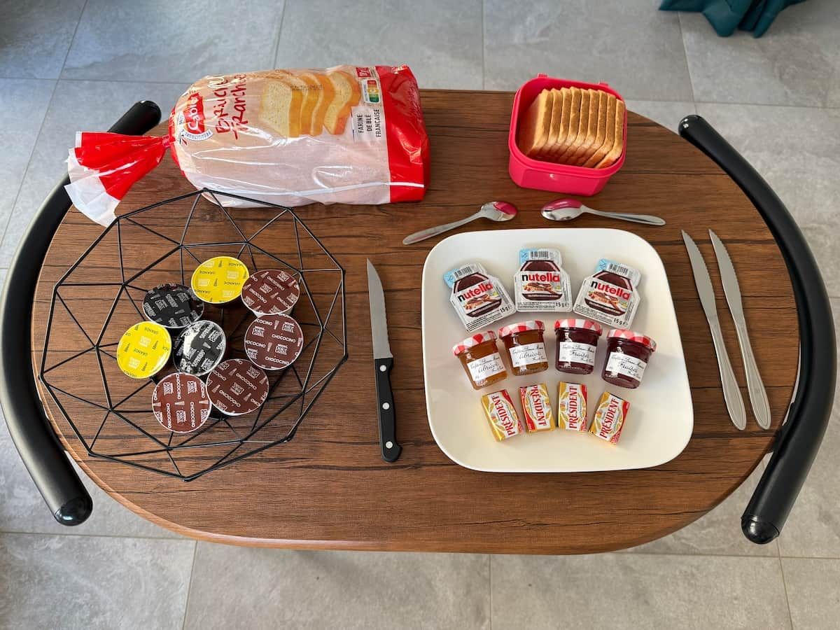 Ein Tisch mit Brot, einer Korb voller Kekse, einer Platte mit Nutella-Gläsern und einem Messer.