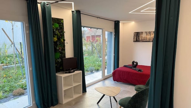 Habitació moderna amb televisió, un sofà vermell, una cadira verda i un finestral gran.