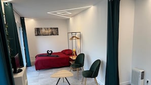 Un dormitori modern amb un llit vermell, una taula auxiliar de fusta, una cadira verda i un radiador.