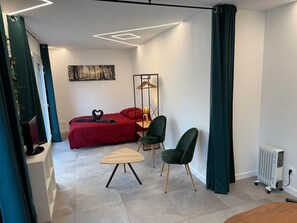 A modern bedroom with a red bed, a wooden side table, a green chair, and a radiator. - defaultName (Besançon)