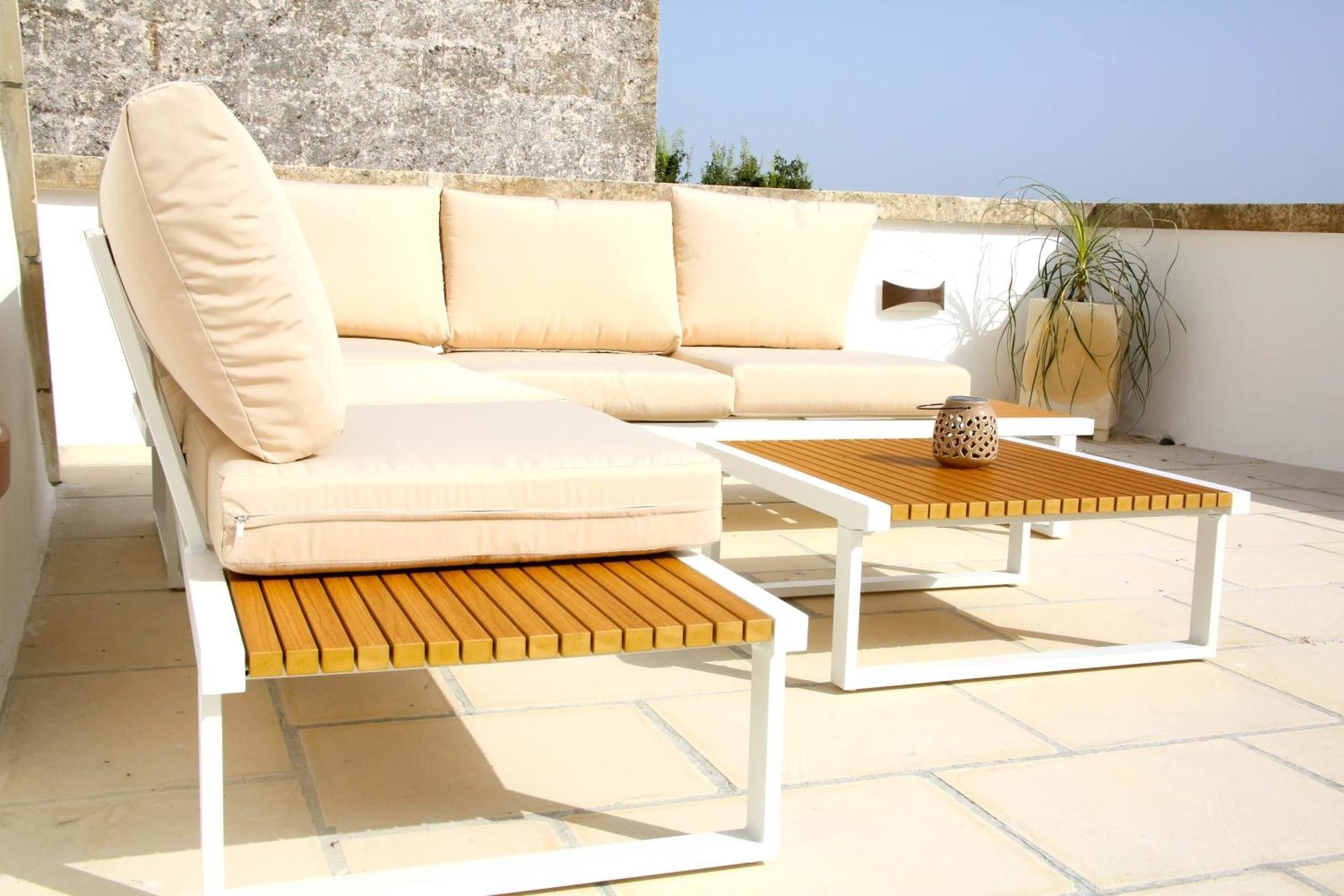 Ein beiges Sofa mit Kissen, ein Holztisch und ein Blumentopf auf einer Terrasses.