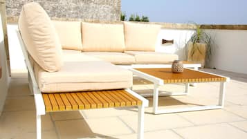Ein beiges Sofa mit Kissen, ein Holztisch und ein Blumentopf auf einer Terrasses.
