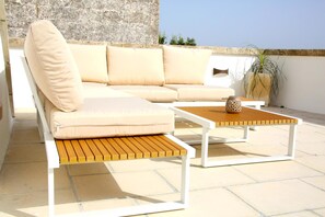 A beige sofa with cushions, a wooden coffee table, and a potted plant on an outdoor patio.