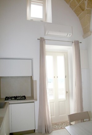 Een compacte kamer met kitchenette, een bed en een deur naar een buitenruimte.