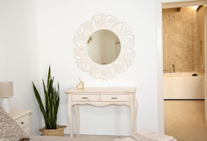 Un bagno con un mobile lavabo bianco, uno specchio rotondo con cornice decorata, una pianta in vaso e una vasca da bagno.