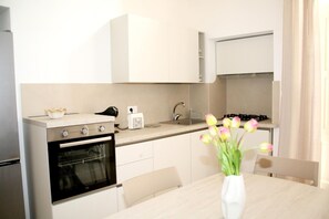 Una cucina moderna con mobili bianchi, un fornello, un forno, un lavello e un vaso con fiori sul tavolo.