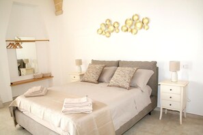 A bedroom with a bed, two bedside tables, a mirror, a wall art piece, and a hanging light fixture.