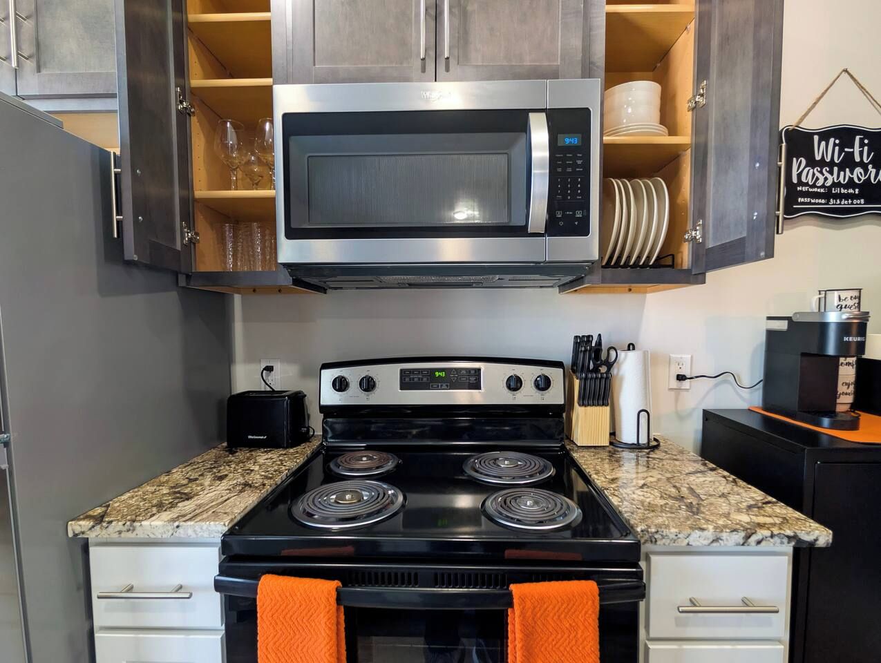 A kitchen with a stainless steel microwave, a black stove with four burners, and wooden cabinets above the counter.