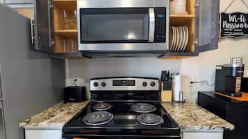 A kitchen with a stainless steel microwave, a black stove with four burners, and wooden cabinets above the counter.