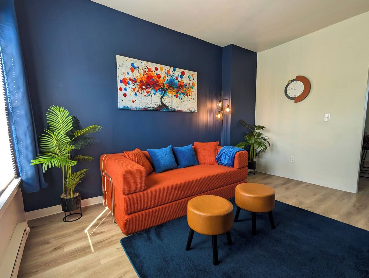 Una sala de estar moderna con un sofá, dos otomanas, un cuadro y un reloj en la pared.