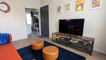 A living room with a sofa, two ottomans, a coffee table, and a flat-screen TV.