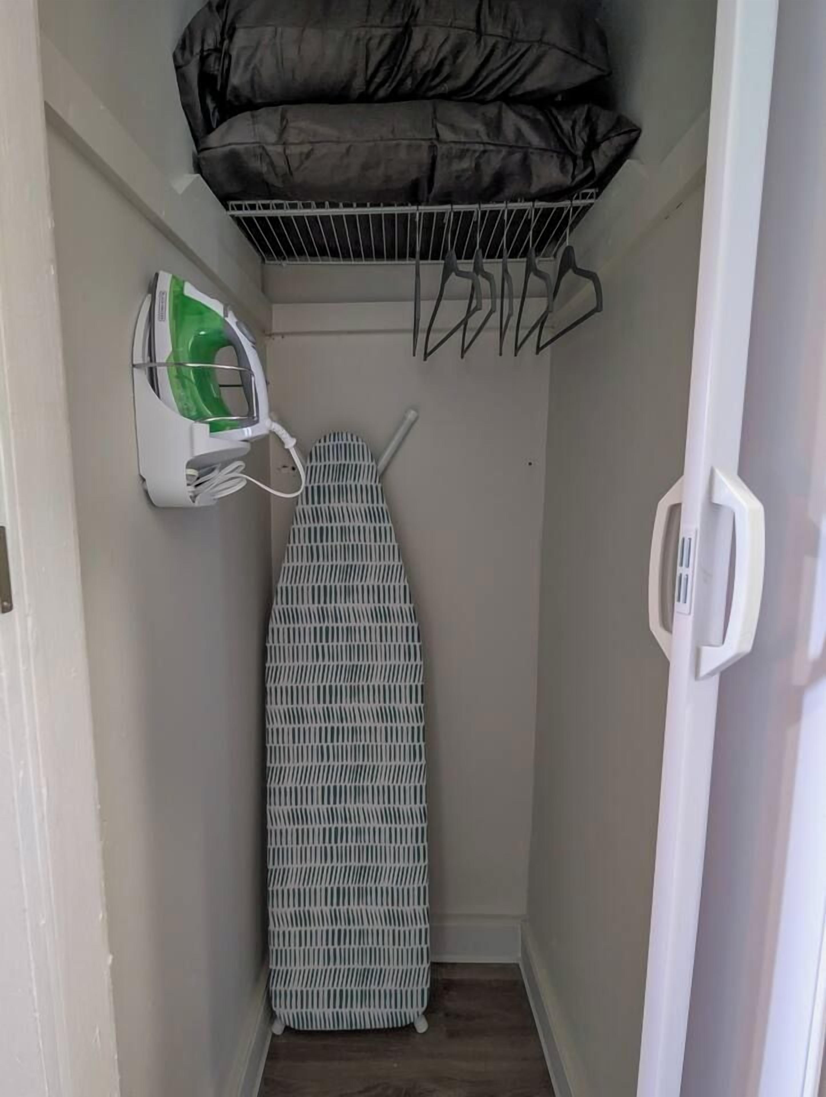A narrow hallway with a wall-mounted ironing board, a hanging laundry rack, and a power outlet with a green appliance plugged in.