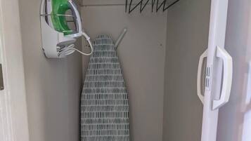 A narrow hallway with a wall-mounted ironing board, a hanging laundry rack, and a power outlet with a green appliance plugged in.