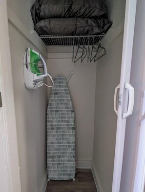 A narrow hallway with a wall-mounted ironing board, a hanging laundry rack, and a power outlet with a green appliance plugged in.