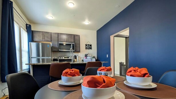 A dining area with round tables, chairs, and a kitchen in the background. - Free Parking | Fast Wi-Fi | DT (Detroit)