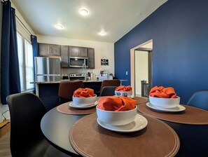 A dining area with round tables, chairs, and a kitchen in the background.