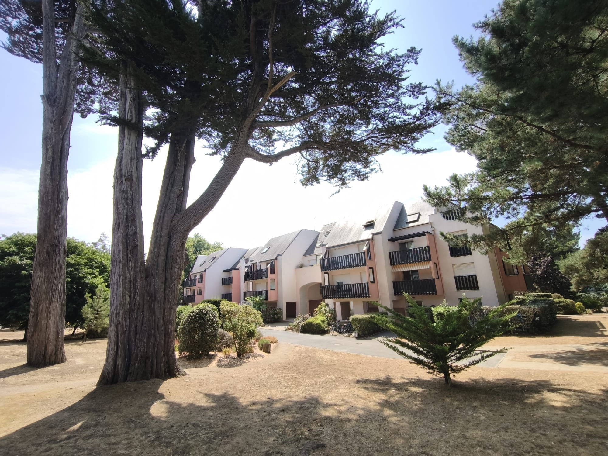 A residential building with multiple balconies, surrounded by mature trees and well-maintained shrubbery.