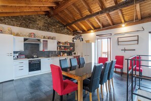 Una cocina moderna con comedor, que presenta una pared de piedra, vigas de madera en el techo y una variedad de electrodomésticos y utensilios de cocina.