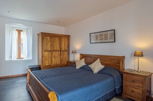 A bedroom with a wooden bed, a nightstand, a lamp, a wardrobe, and a framed certificate on the wall.
