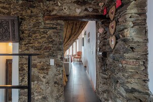 Un pasillo de paredes de piedra con una viga de madera en el techo, que conduce a una habitación con un sofá y una silla.