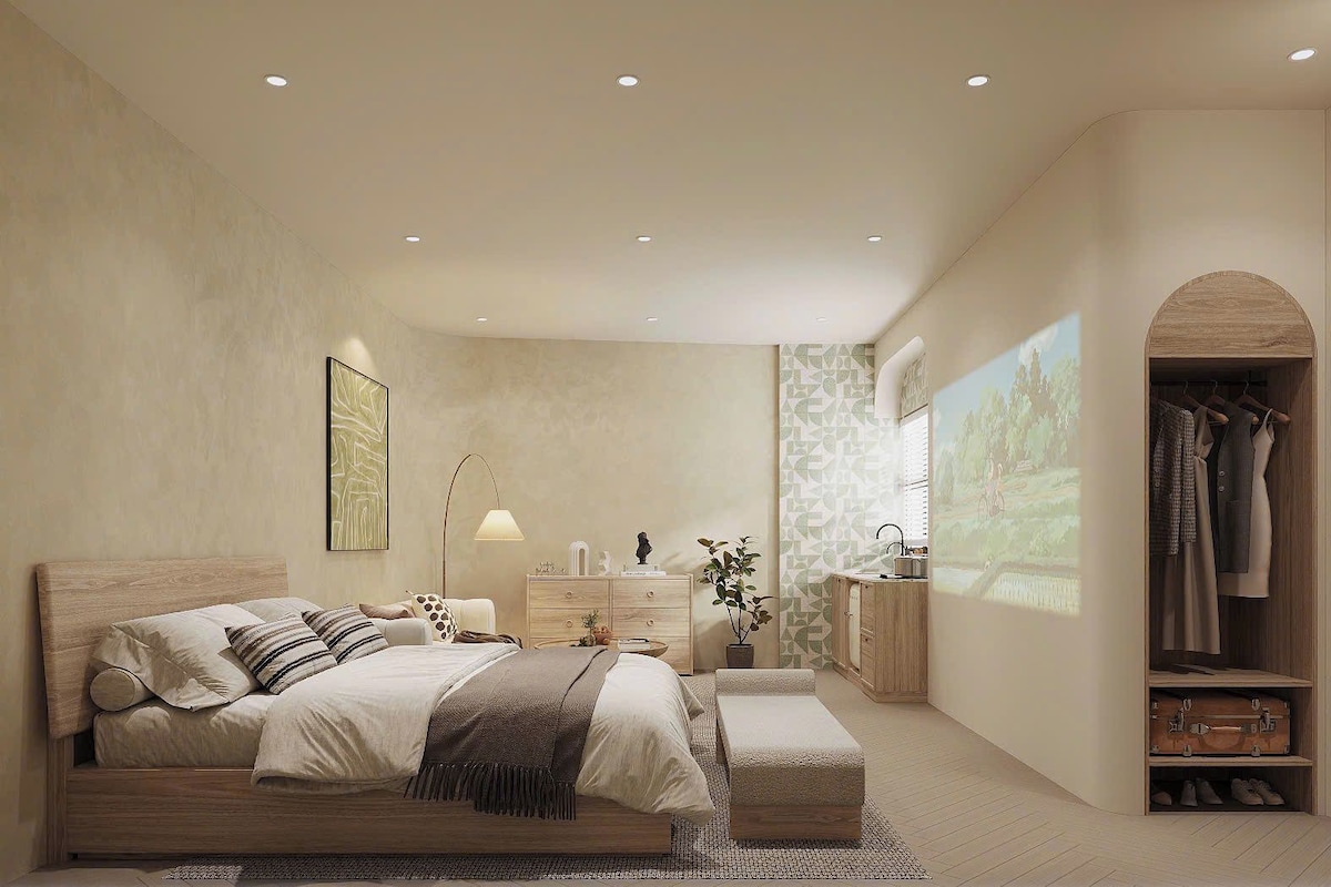 Een slaapkamer met een bed, nachtkastje, lamp, kaptafel en een kledingkast met hangende kleding.
