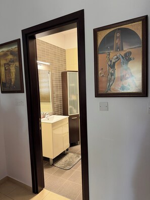 A hallway with a door leading to a kitchen area, a framed artwork on the wall, and a tiled floor. - Villa no7|Private pool,7 min walk to the beach & Four Seasons (Limassol, Agios Tychonas)