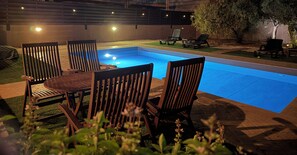 An outdoor swimming pool area with wooden chairs and a table, surrounded by a well-maintained lawn and a wooden fence. - Villa no7|Private pool,7 min walk to the beach & Four Seasons (Limassol, Agios Tychonas)