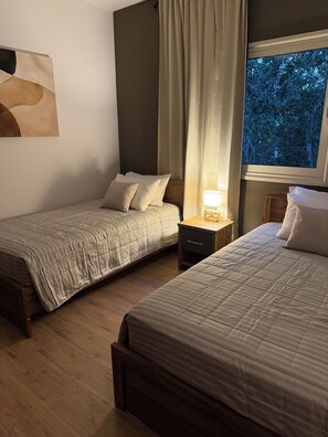 A hotel room with two beds, a nightstand with a lamp, a window with a view of trees, and a wall-mounted abstract painting. - Villa no7|Private pool,7 min walk to the beach & Four Seasons (Limassol, Agios Tychonas)