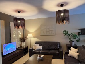A modern living room with a leather sofa, a coffee table, a TV, and decorative plants. - Villa no7|Private pool,7 min walk to the beach & Four Seasons (Limassol, Agios Tychonas)