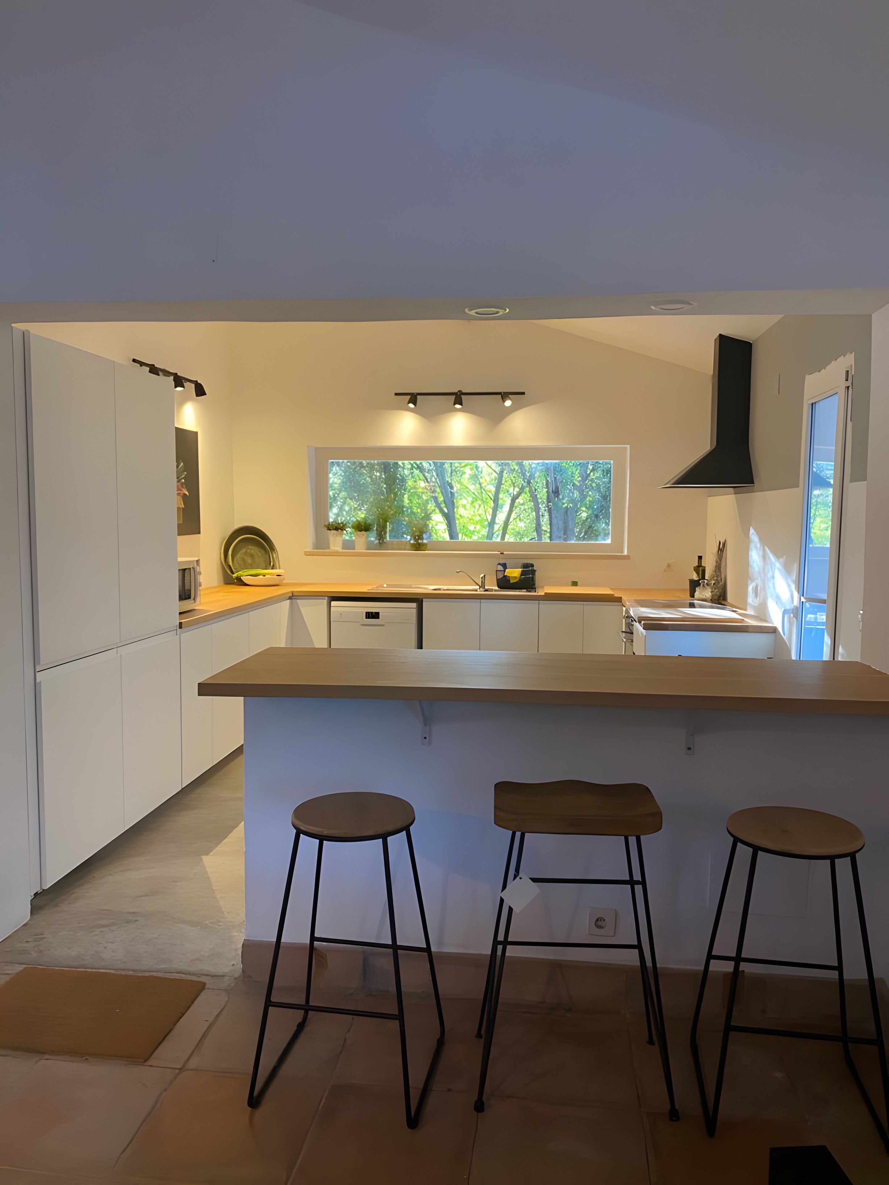 Une cuisine moderne dotée d’une grande fenêtre, de deux tabourets de bar et d’un four encastré.