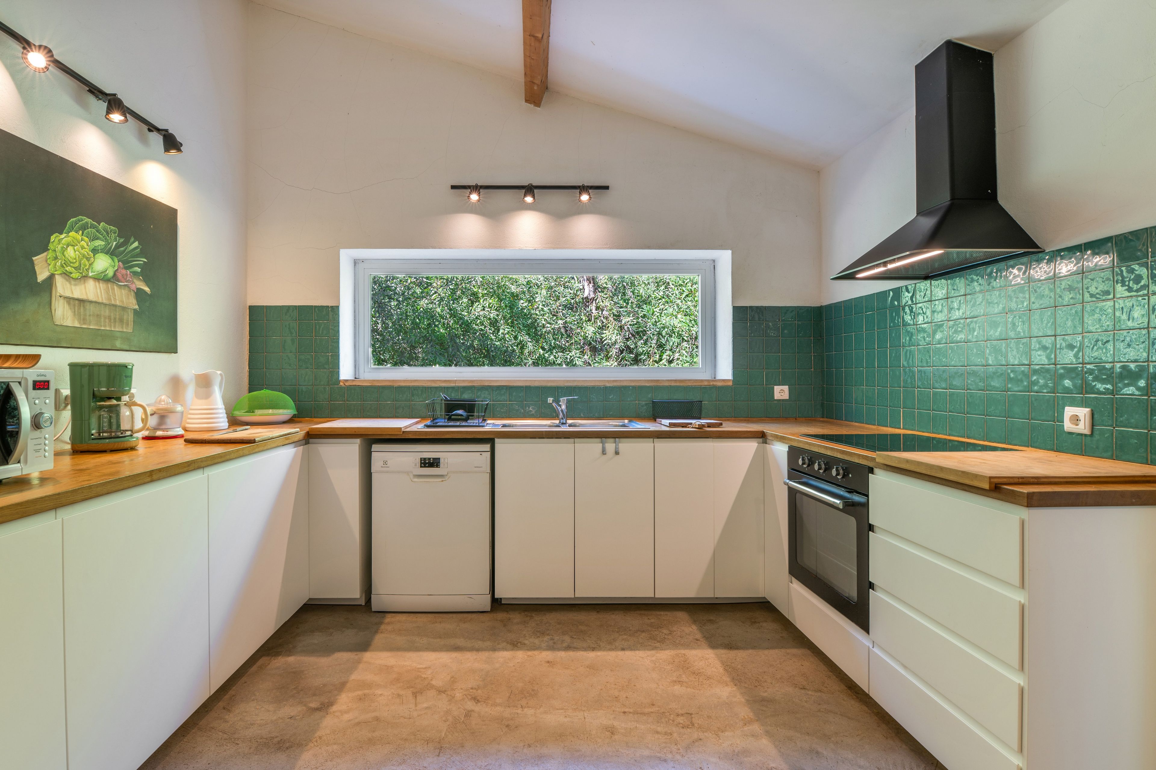 Una cocina con ventana, baldosas verdes, lavavajillas y estufa.