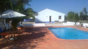 A swimming pool with a tiled deck, a white building with a door and windows, and outdoor furniture including chairs and a table. - Country House 'Monte Do Campaniço' with Mountain View, Private Pool and Wi-Fi (Tanganheira)