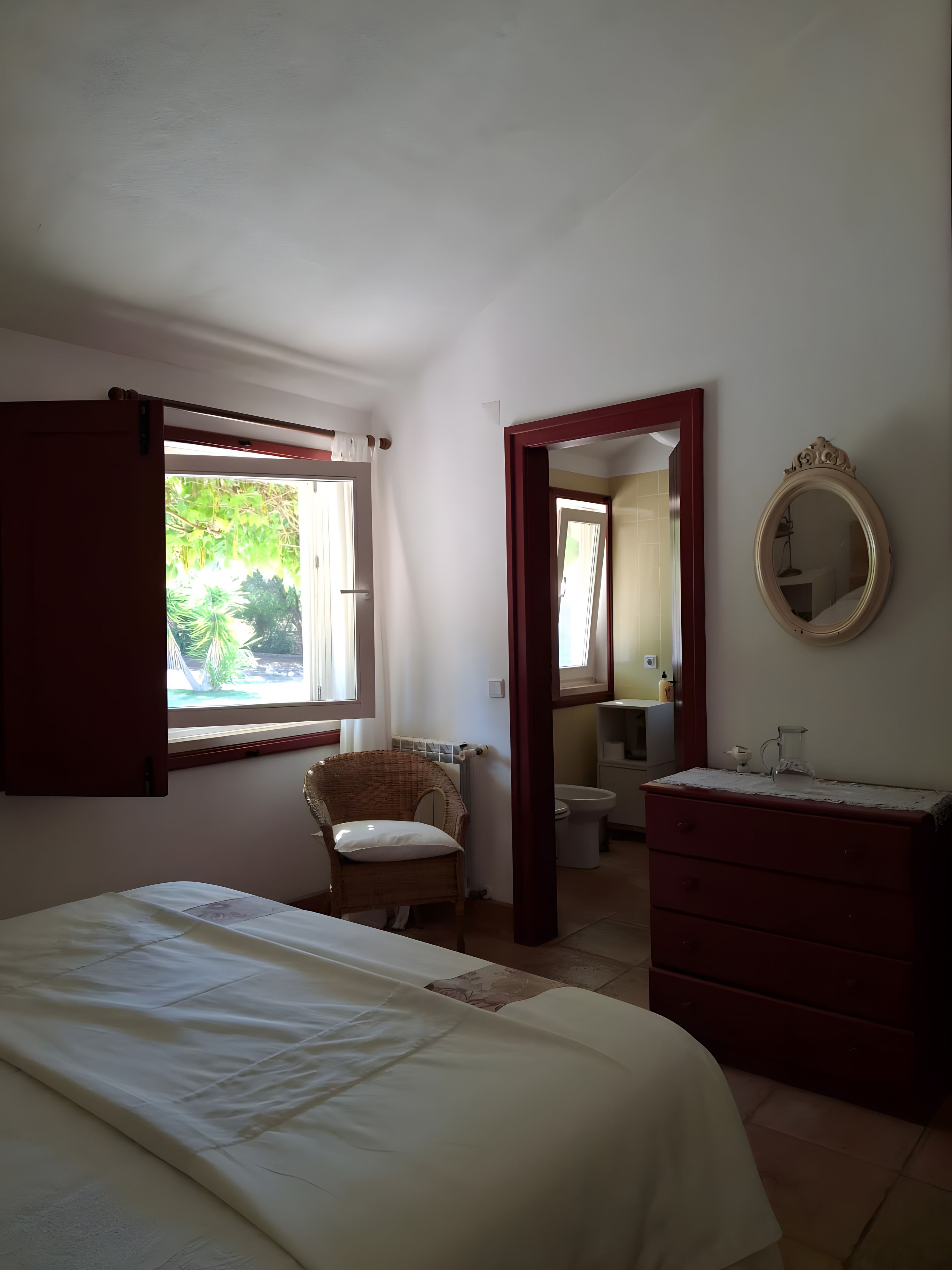 A bedroom with a bed, a chair, a dresser, and a bathroom visible through an open door.