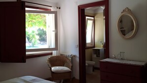 A bedroom with a bed, a chair, a dresser, and a bathroom visible through an open door. - Country House 'Monte Do Campaniço' with Mountain View, Private Pool and Wi-Fi (Tanganheira)
