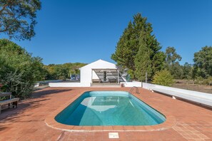 En swimmingpool med en vit byggnad i bakgrunden, omgiven av träd och en klar himmel.