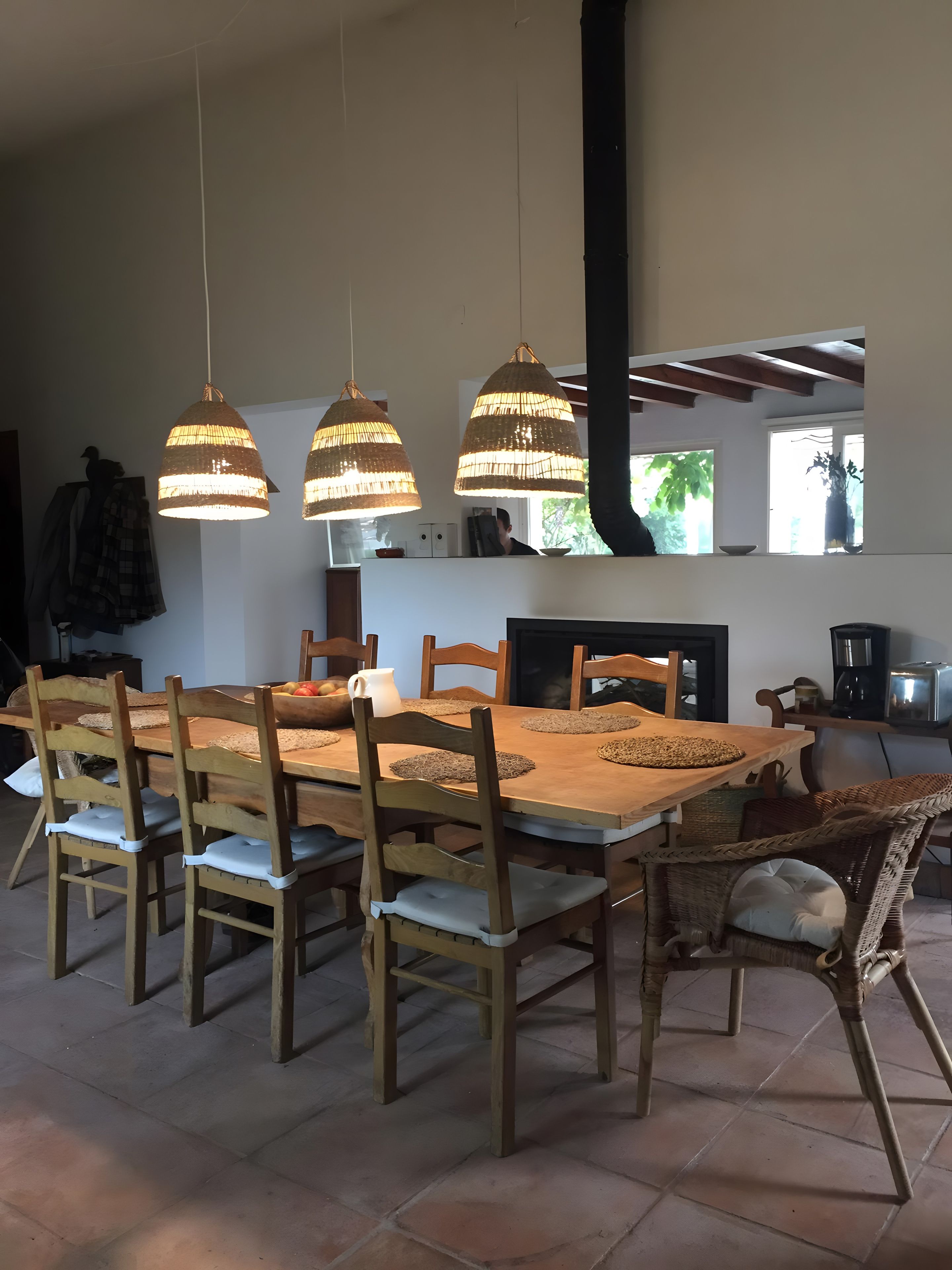 A dining area with a wooden table and chairs, pendant lights, and a view of the outdoors.