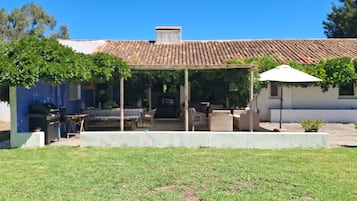 A covered outdoor seating area with chairs and a table, a barbecue grill, and a potted plant.