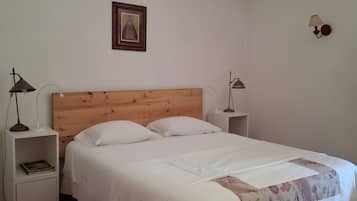 A bedroom with a wooden headboard, white bedding, a red throw blanket, and a framed picture on the wall.