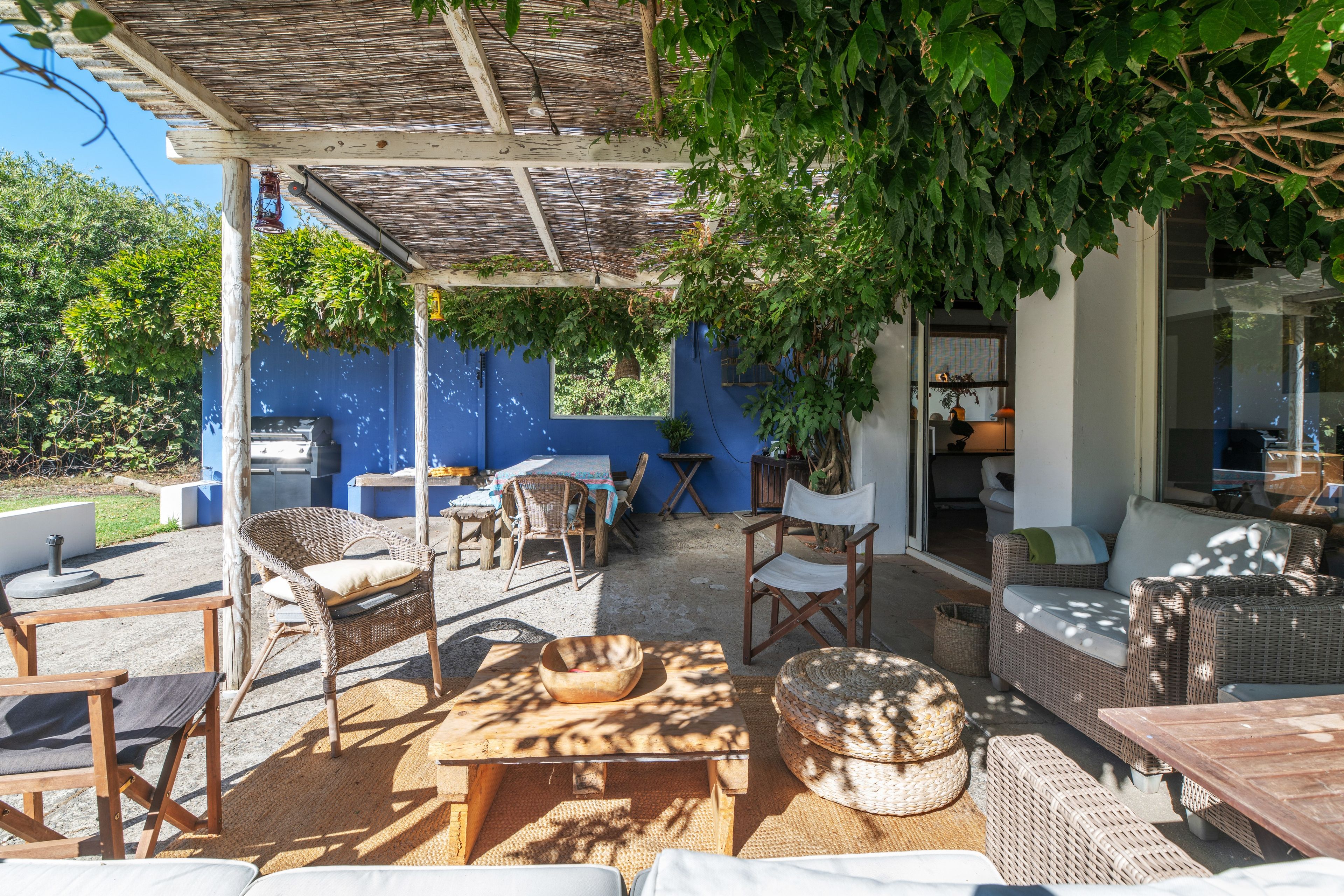 Un patio al aire libre con mobiliario de mimbre, una pared azul y una pérgola cubierta de hiedra.