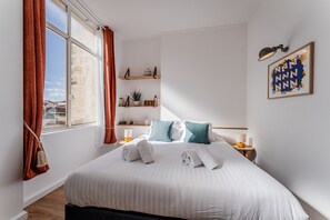 A hotel room with a large bed, two bedside tables, a window with curtains, a wall-mounted shelf with decorative items, and a framed artwork. - Triangle d'Or — Elegance & King Size bed (Bordeaux)