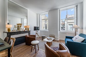 A modern living room with a dining area, a large mirror, and a view of the cityscape through the windows. - Triangle d'Or — Elegance & King Size bed (Bordeaux)