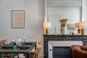 A dining area with a table set for four, a fireplace with two lamps, and a framed quote on the wall. - Triangle d'Or — Elegance & King Size bed (Bordeaux)